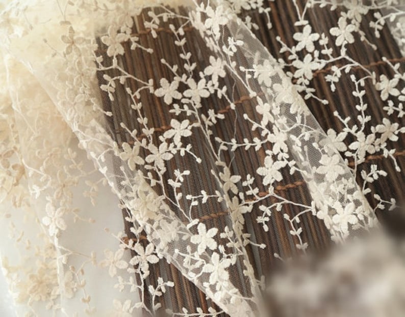 May include: Close-up of ivory lace fabric with a delicate floral pattern. The lace is sheer and has a soft, romantic feel.