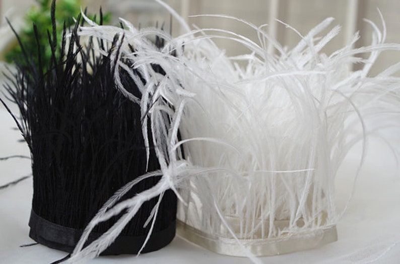 May include: Two bundles of ostrich feathers, one black and one white, are tied together with a black ribbon. The feathers are soft and fluffy, and they would be perfect for a craft project or a decorative accent.