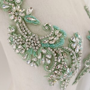 May include: A delicate floral applique with a mint green and silver design. The applique is made of rhinestones and beads, and it is perfect for adding a touch of elegance to any garment.