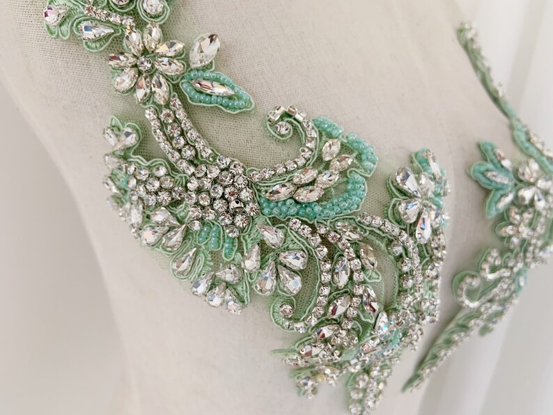 May include: A delicate floral applique with a mint green and silver design. The applique is made of rhinestones and beads, and it is perfect for adding a touch of elegance to any garment.
