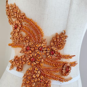 May include: A large, orange and red beaded applique with a floral design. The applique is made of small, iridescent beads and sequins.