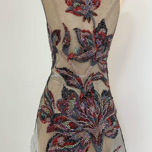 May include: A sheer black mesh fabric panel featuring intricate floral embroidery and embellishments. The design consists of large, detailed flowers and leaves crafted with iridescent red, purple, and dark grey beads and sequins throughout.