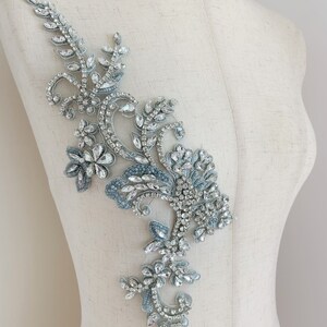 May include: A silver and blue beaded applique with a floral design. The applique is made with rhinestones and beads and is perfect for adding a touch of sparkle to any garment.