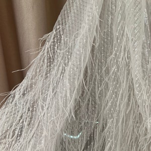 Puede incluir: Tela de ribete de plumas blancas con un delicado patr&oacute;n brillante. La tela tiene una textura suave y fluida, perfecta para agregar un toque de elegancia a cualquier proyecto.