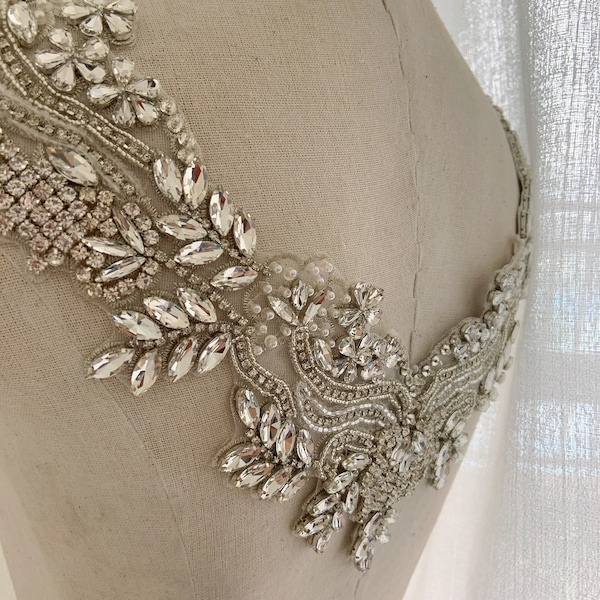 May include: A delicate, beaded and crystal embellished neckline applique for a wedding dress or other formal garment. The applique features a V-shaped design with a floral motif and clear crystals.