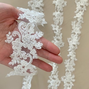 May include: White lace trim with a floral design and small pearl accents. The lace is delicate and intricate, and would be perfect for adding a touch of elegance to any project.