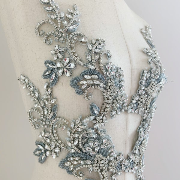 May include: A silver and blue beaded and sequined applique with a floral design. The applique is on a white mannequin.