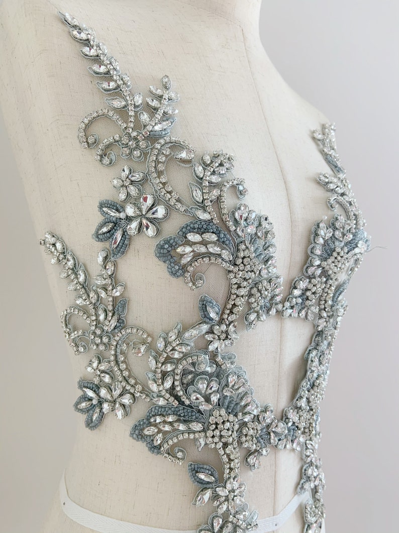 May include: A silver and blue beaded and sequined applique with a floral design. The applique is on a white mannequin.