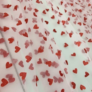 May include: Pink tulle fabric with a scattered pattern of red glitter hearts.