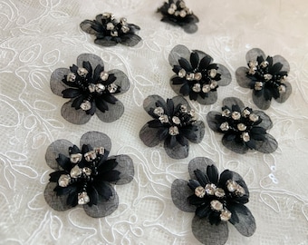 May include: Black fabric flower embellishments with rhinestones. Each flower has a layered fabric design and is decorated with sparkling rhinestones.