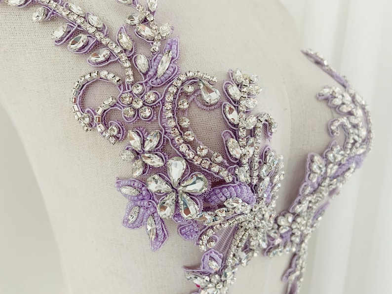 May include: A delicate lavender and silver beaded applique with rhinestones. The applique features a floral design with intricate details.