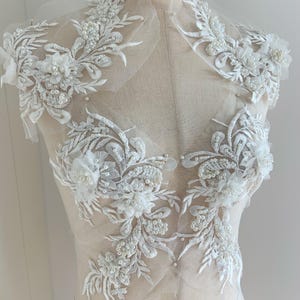 Puede incluir: Aplique de encaje blanco con adornos de perlas. El encaje presenta diseños florales y abalorios delicados. Este aplique es perfecto para añadir un toque de elegancia a cualquier prenda.