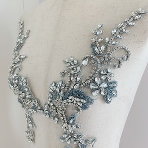 May include: A silver and blue beaded applique with a floral design. The applique is made with rhinestones and beads and is perfect for adding a touch of sparkle to any garment.