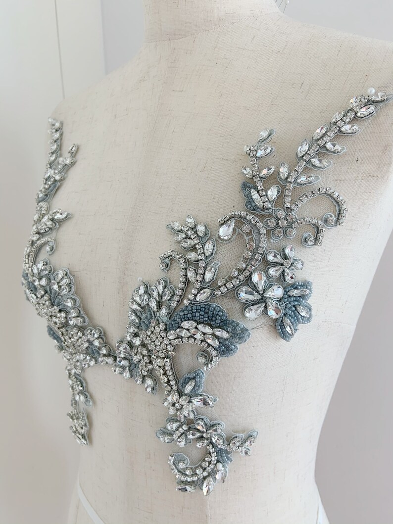 May include: A silver and blue beaded applique with a floral design. The applique is made with rhinestones and beads and is perfect for adding a touch of sparkle to any garment.