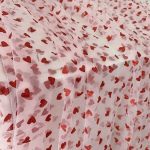 May include: Pink tulle fabric with a red glitter heart pattern. The fabric is sheer and delicate.