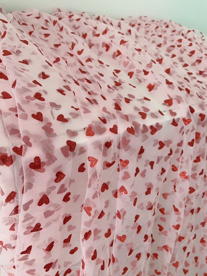May include: Pink tulle fabric with a red glitter heart pattern. The fabric is sheer and delicate.