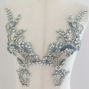 May include: A pair of silver and blue beaded appliques with a floral design. The appliques are made with rhinestones and beads and are perfect for adding a touch of sparkle to any garment.