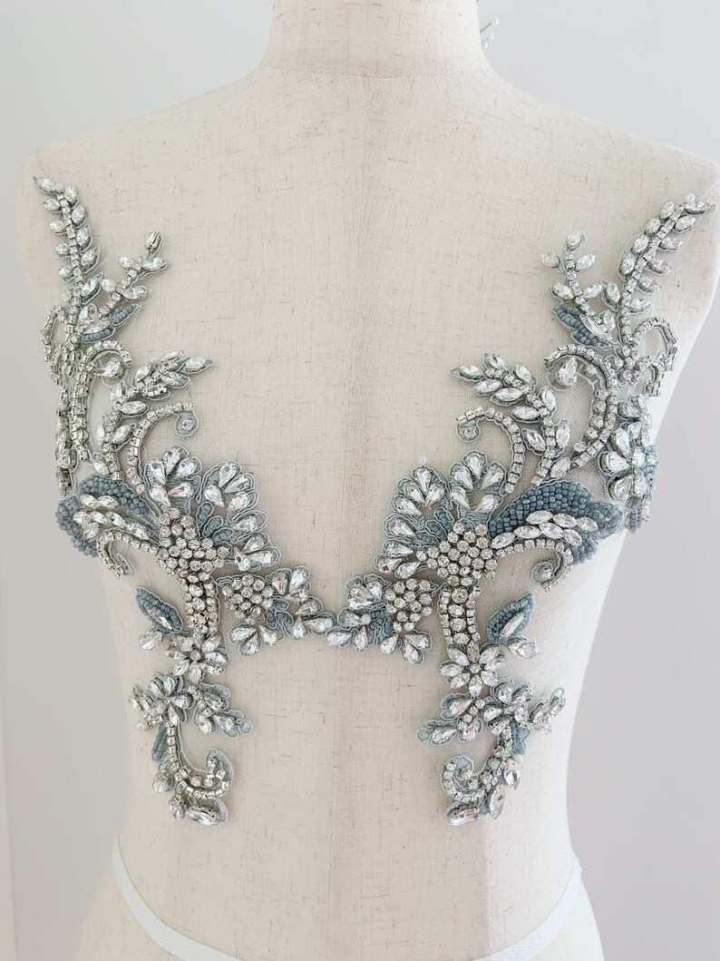 May include: A pair of silver and blue beaded appliques with a floral design. The appliques are made with rhinestones and beads and are perfect for adding a touch of sparkle to any garment.
