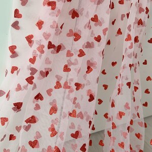May include: Pink sheer fabric with a red glitter heart pattern. The fabric is folded in half and the hearts are visible on both sides.