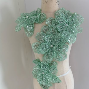 May include: Four light green beaded floral appliques with crystal centres, arranged on a dress form.