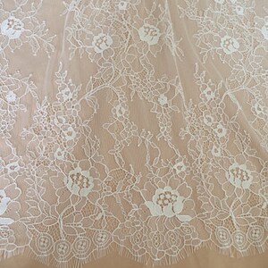 May include: White floral lace fabric with a delicate pattern. The lace has a scalloped edge and is perfect for crafting, sewing, or adding a touch of elegance to any project.