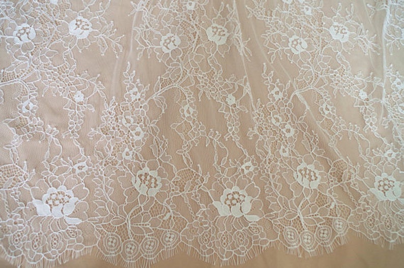 May include: White floral lace fabric with a delicate pattern. The lace has a scalloped edge and is perfect for crafting, sewing, or adding a touch of elegance to any project.
