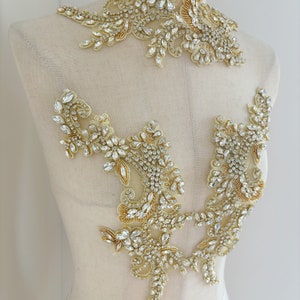 May include: Two gold and crystal beaded appliques for clothing or crafts. The larger applique is a floral design with a curved shape. The smaller applique is a more symmetrical floral design.
