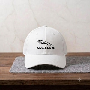 May include: A white baseball cap featuring the black Jaguar logo and the word JAGUAR printed in black text on the front panel. The cap has a structured crown, a curved brim, and stitched eyelets on the top panels for ventilation and durability.
