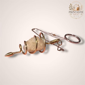 May include: A clear, rough-cut quartz crystal encased in a spiraling gold-toned metal wire cage. The crystal is attached to a delicate gold-toned chain that connects to a circular metal keyring, creating a decorative pendant or keychain accessory.