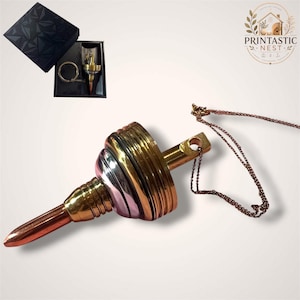 Peut inclure: Un pendentif métallique en forme de fil à plomb, doté d'une pointe cuivrée, d'une section centrale dorée avec des stries horizontales et d'une bande argentée. Une fine chaîne à billes de couleur cuivre est fixée à l'anneau supérieur.