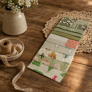 May include: A stack of rectangular fabric swatches featuring various green, white, and red patterns, including floral, geometric, and animal motifs. The swatches are arranged in a vertical column on a crocheted lace mat next to a ceramic pitcher.