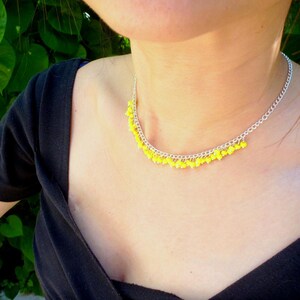 May include: A silver chain necklace with yellow beads dangling from it. The necklace is worn by a person with a black shirt.