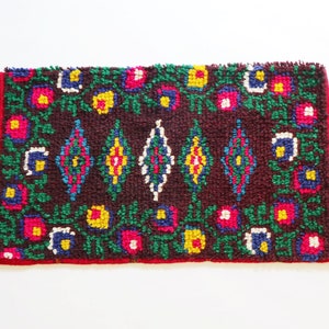 May include: A small, rectangular rug with a brown background and a colorful geometric pattern. The rug has a red border and features green, yellow, blue, and pink accents.