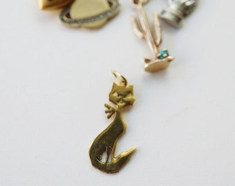 May include: A gold charm in the shape of a cat. The cat is sitting with its tail curled around its body. The charm is part of a charm bracelet.