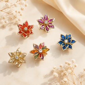 May include: Five flower-shaped brooches with gold-tone metal frames and multi-colored petals. Each brooch features a central clear crystal. The colors include red, purple, blue, clear, and a multi-colored rainbow arrangement of petals.