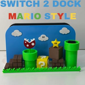 Può includere: Una docking station blu per console di gioco con design a tema Mario, dotata di tubi verdi, blocchi di mattoni marroni, un blocco giallo con punto interrogativo, una pianta piranha rossa e bianca, una stella gialla e nuvole bianche.