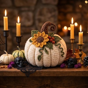 May include: A cream-colored crocheted pumpkin featuring a brown curly stem, a yellow sunflower, green leaves, and small red berries. The pumpkin is surrounded by lit beeswax candles in metal holders, black skulls, pinecones, and small pumpkins.