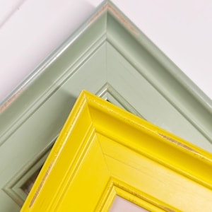 Può includere: Due cornici rettangolari sovrapposte con un profilo a gradini. La cornice superiore è di colore giallo brillante, mentre quella inferiore è di un verde salvia tenue. Entrambe le cornici presentano segni di usura visibili lungo i bordi.