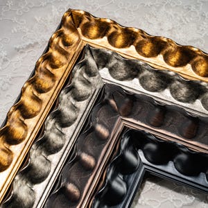 May include: A set of four nested picture frames featuring a wavy, scalloped edge design. The frames are finished in metallic gold, silver, bronze, and matte black, each displaying a consistent undulating pattern along the outer border.