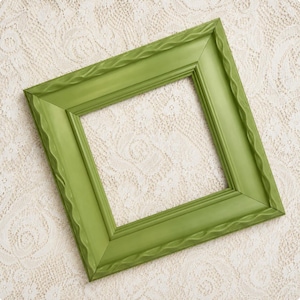 May include: A square picture frame in a matte olive green finish. The frame features a wide, flat border with a decorative, wavy, rope-like molding detail running along the inner and outer edges, creating a textured appearance on the surface.