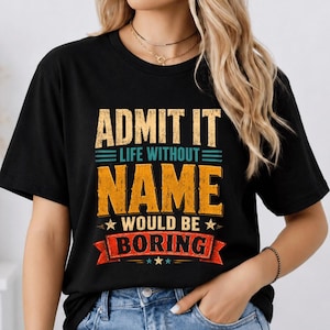 Puede incluir: Una camiseta negra de manga corta con el texto ADMIT IT LIFE WITHOUT NAME WOULD BE BORING en una tipografía desgastada de color amarillo, verde azulado y rojo. El diseño incluye líneas horizontales, estrellas pequeñas y una pancarta.