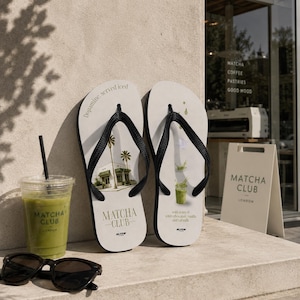 May include: A pair of white flip-flops with black straps featuring Matcha Club branding. The left sandal displays a building and palm trees with the text dopamine. served iced. The right sandal shows a matcha drink with text notes of white chocolate, vanilla and oat milk.