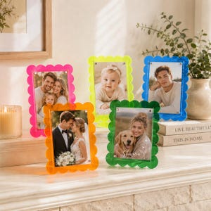 May include: Four scalloped acrylic picture frames in neon pink, bright yellow, vibrant orange, and emerald green. Each frame holds a photograph, including portraits of a family, a baby, a man, a couple at a wedding, and a person with a dog.