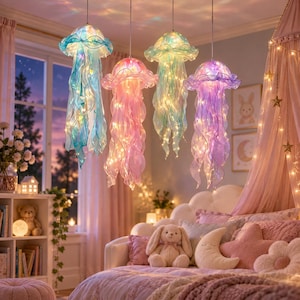 May include: Four hanging jellyfish-shaped pendant lights with translucent, ruffled fabric shades in blue, pink, green, and purple. Each light features internal string lights that emit a warm glow, suspended from the ceiling by thin, metallic cords.