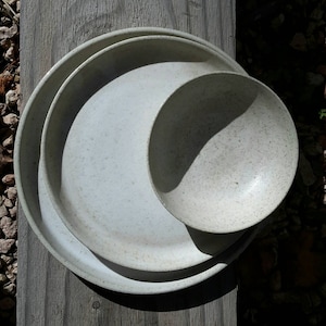May include: Three white ceramic bowls with a speckled glaze. The bowls are nested together, with the largest bowl on the bottom and the smallest bowl on top.