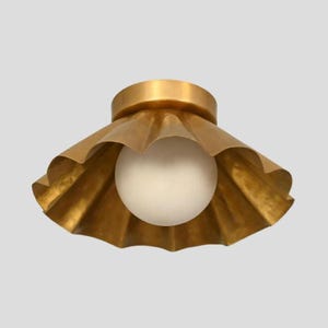 Può includere: Una plafoniera a incasso caratterizzata da un ampio paralume in ottone smerlato con finitura metallica spazzolata. Al centro del paralume si trova una singola lampadina sferica in vetro bianco satinato che diffonde una luce morbida.
