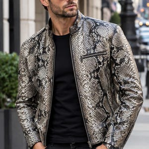 May include: A long-sleeve jacket featuring a grey and black snakeskin pattern, a stand-up collar, a full-length front zip, and a zipped chest pocket. The jacket is worn over a plain black t-shirt and paired with dark grey denim jeans.
