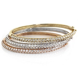 Può includere: Quattro braccialetti rigidi in oro, argento e oro rosa. Ogni braccialetto è adornato con una fila di pietre preziose chiare e scintillanti. I braccialetti sono impilati, mostrando i loro diversi colori e design. I gioielli sono su sfondo bianco.
