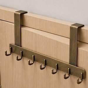 Könnte beinhalten: Eine Türgarderobe mit gebürstetem Antik-Messing-Finish. Der Metall-Organizer besteht aus zwei vertikalen Halterungen, die über die Oberkante einer Tür greifen, und einer horizontalen Leiste mit sieben gleichmäßig verteilten J-förmigen Haken.