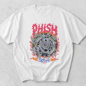 May include: A white short-sleeve t-shirt featuring a graphic print of a spiraling gray structure surrounded by pink flames. The text reads PHISH at the top and Sphere 2026 at the bottom, with smaller text reading Nine Nights at Las Vegas NV.
